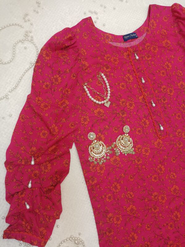 Vibrant pink floral 2-piece co-ord set with puff sleeves and pearl button detailing, laid flat with pearl accessories.